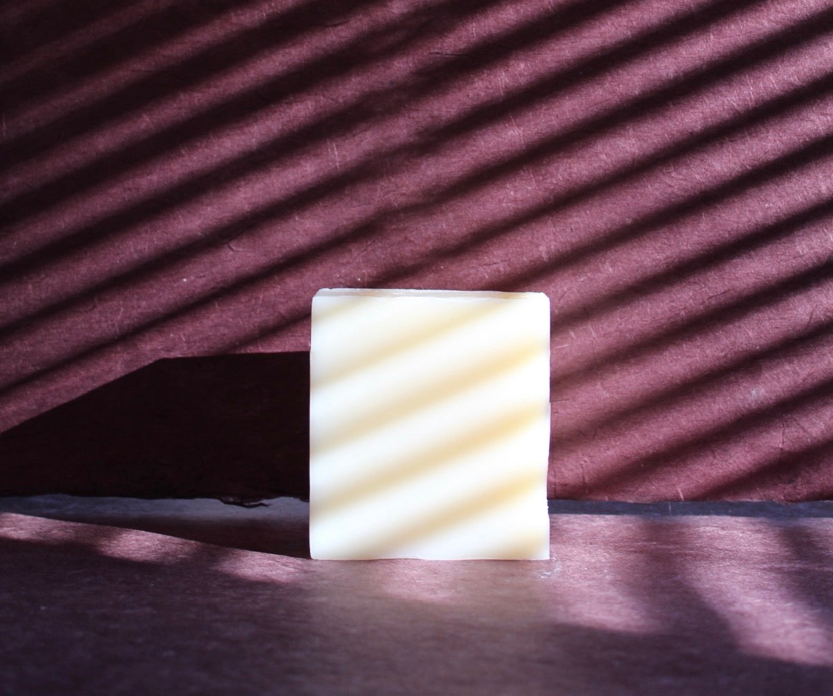 Collection of Natural bar soaps with grapes, plants, cut fruit, and sunflower with whitewashed wooden structure in background.