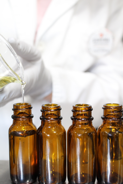 dark glass bottle with white label and dropper containing oil with cut fruit, and a carrot on a whitewashed wooden board.