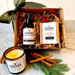 Do Not Disturb gift set displayed decoratively with a bow, evergreen, and cinnamon sticks — includes body oil, scrub soap, and grapefruit lemongrass candle for a cozy self-care night.